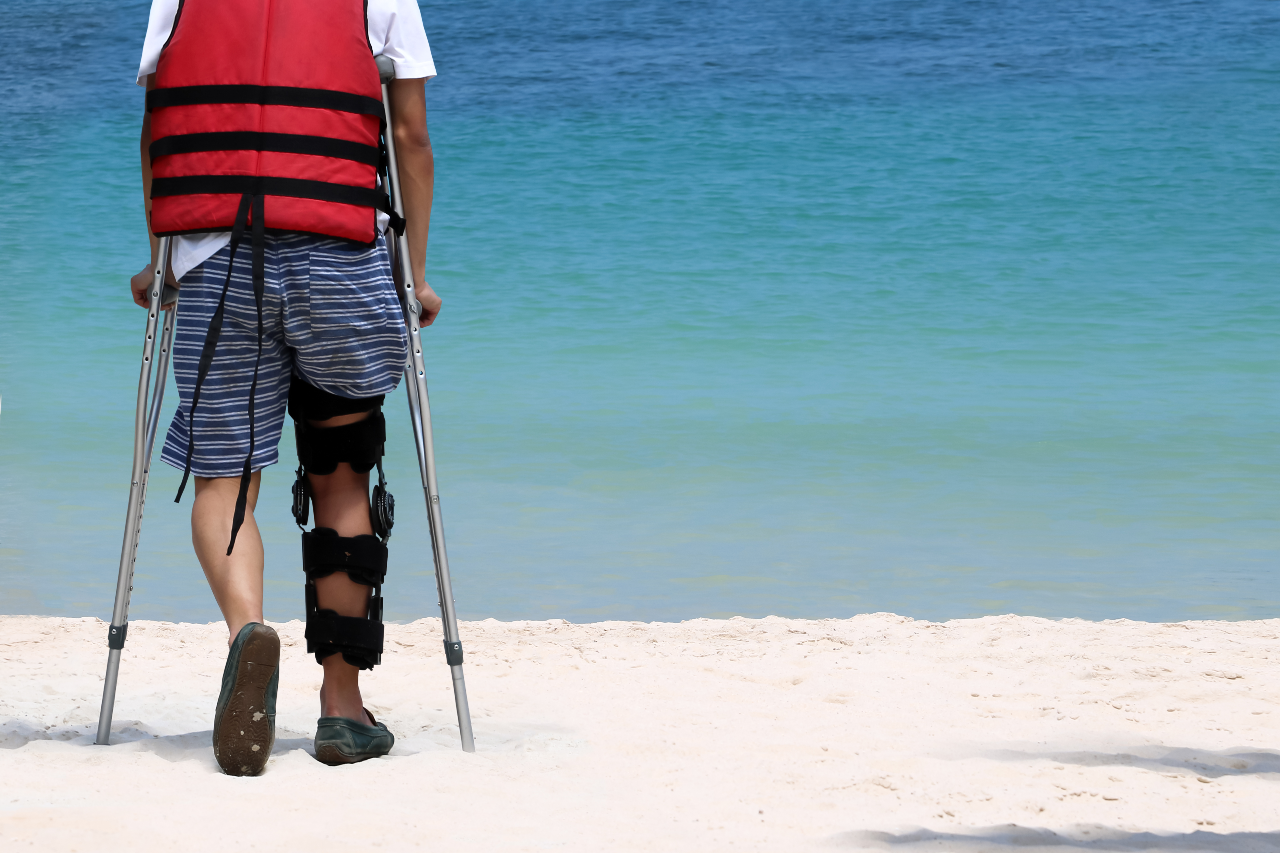 man with crutches with a leg injury at the beach