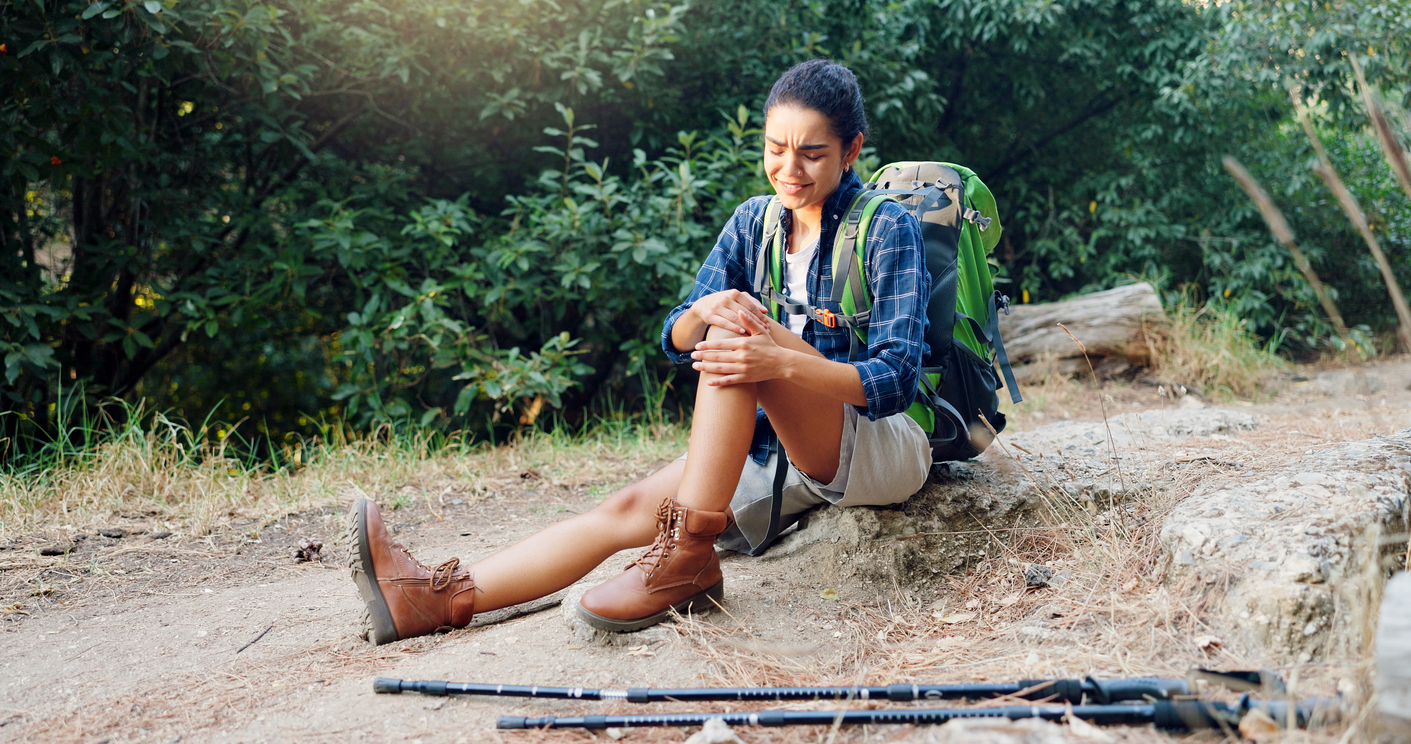 Hiker Sitting On The Ground Grabbing Her Knee In Pain