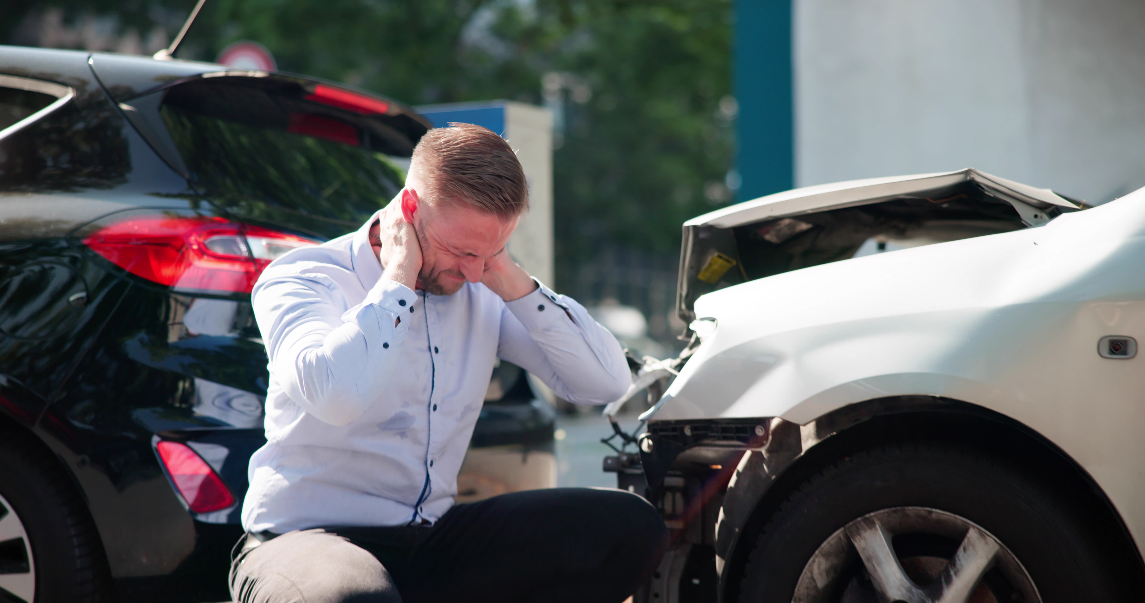 Man Holding Neck and Crouching In Front of Car Accident
