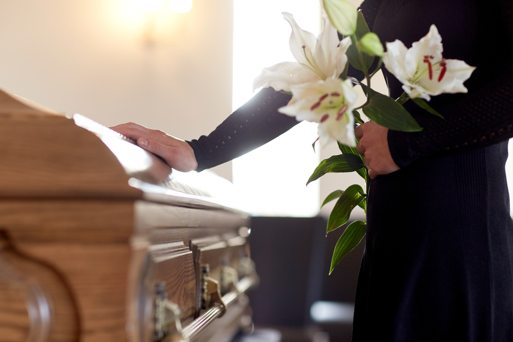 man at a funeral holding white lilies with hand on casket