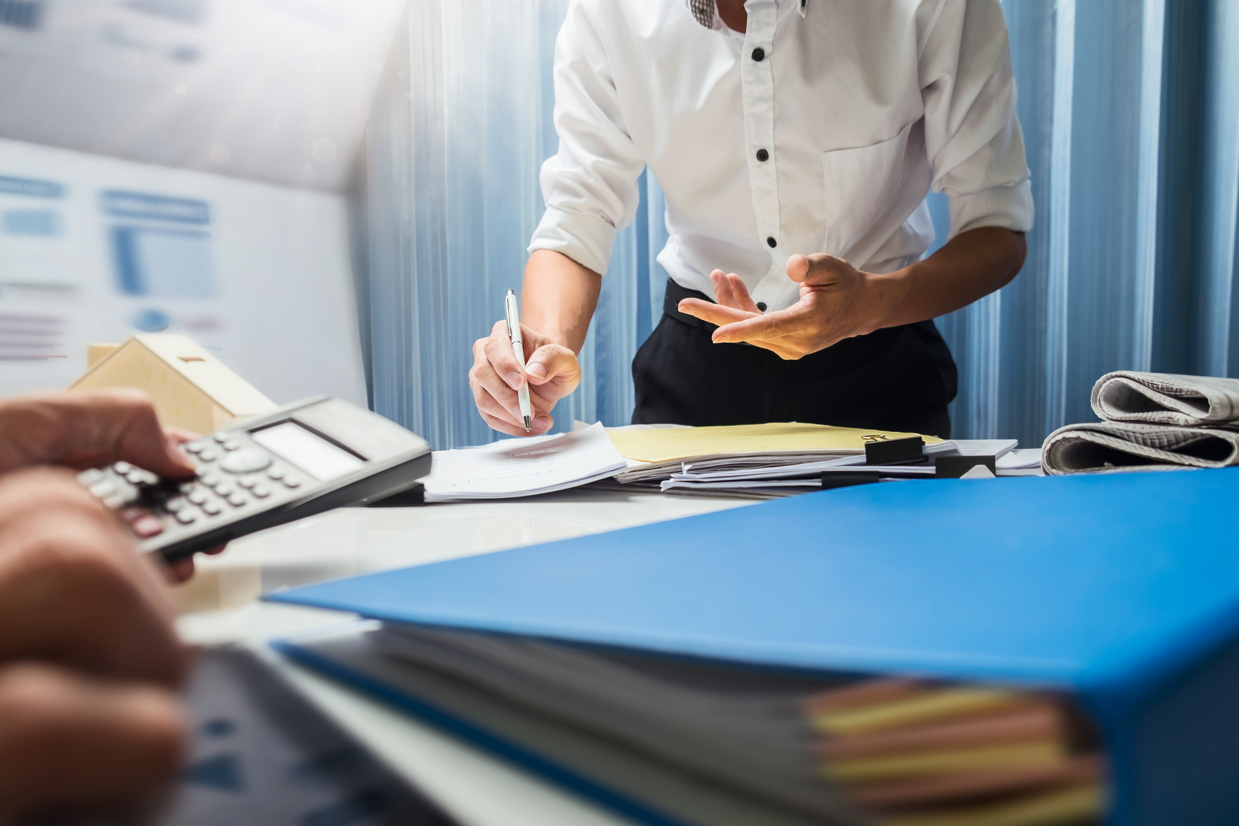 person standing over paperwork and another with a calculator